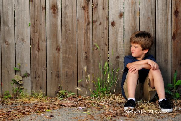 Boy sitting along a wooden fence: Advice for simplifying homeschooling from Simply Homeschool